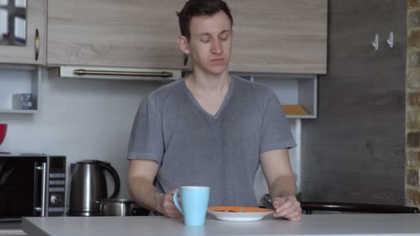 Young man eating oatmeal porridge and coffee in the kitchen — Stock Video