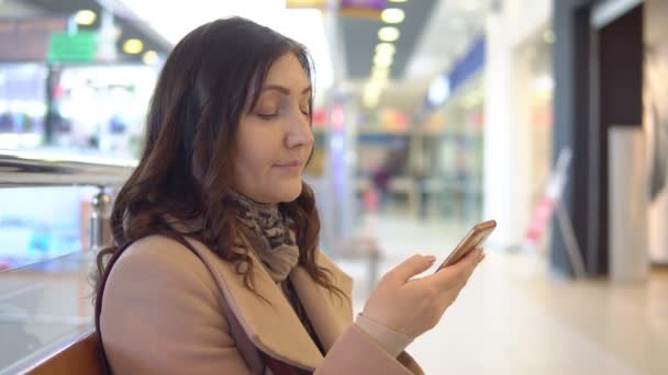 Νεαρή γυναίκα σε ένα εμπορικό κέντρο με ένα τηλέφωνο — Αρχείο Βίντεο