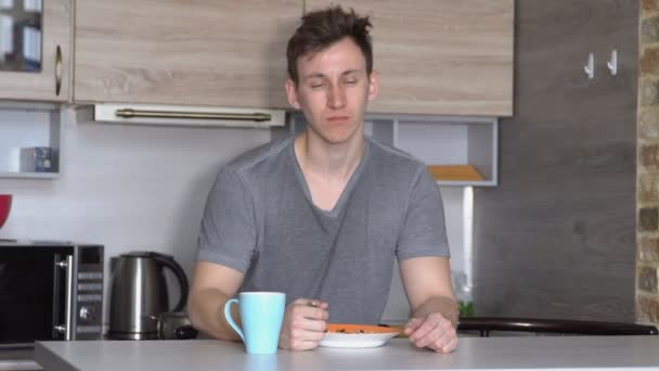 Hombre guapo se queda dormido en la mesa del desayuno en la cocina — Vídeo de stock