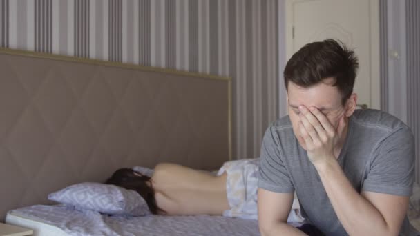 Man zit op een bed tegen de achtergrond van een naakte dames terug — Stockvideo