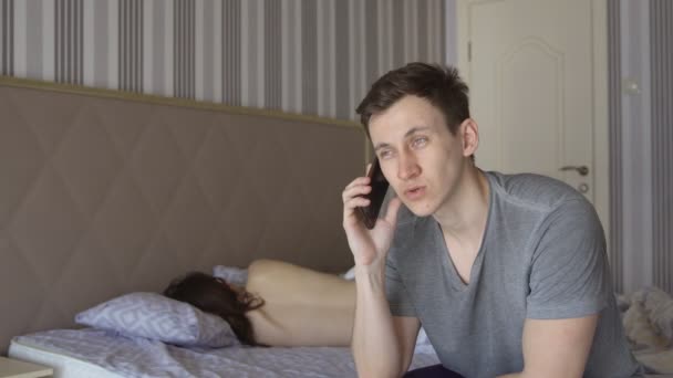남자는 벌 거 벗은 여자의 배경에 전화와 침대에 앉아 — 비디오