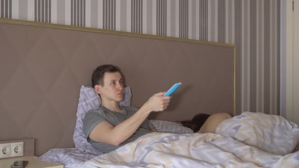 Homme avec télécommande et femme nue allongée sur le lit — Video