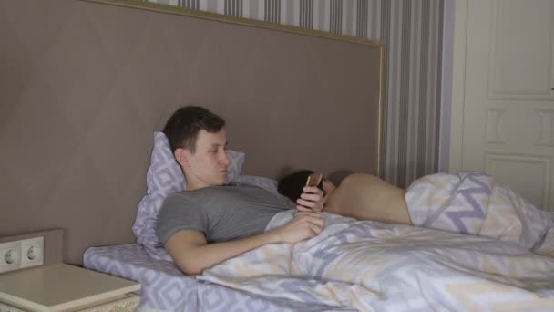 Hombre con teléfono y mujer desnuda acostada en la cama — Vídeos de Stock