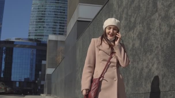 Mujer en un abrigo va al centro de la ciudad, hablando por teléfono — Vídeo de stock