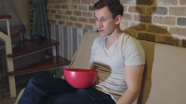 Hombre guapo con una cerveza y patatas fritas delante de la televisión — Vídeo de stock