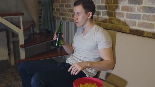 El hombre bebe cerveza y patatas fritas delante de la televisión viendo fútbol — Vídeo de stock