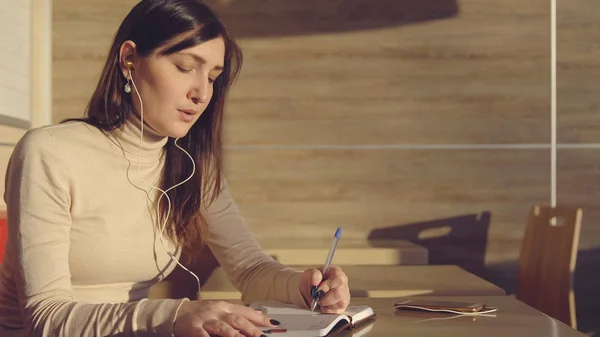 Mujer Joven Sentada Cafetería Con Auriculares Tomando Notas Cuaderno —  Fotos de Stock