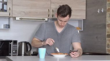 Mutfakta bir masada bir telefon ile genç adam yiyor