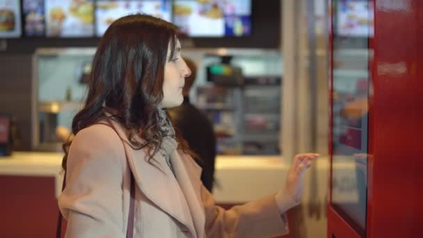 Красива жінка брюнетка в пальто накази продовольства через термінал — стокове відео