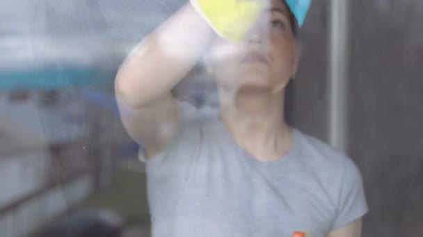 Женщина в жёлтых перчатках моет окно синей тряпкой — стоковое видео