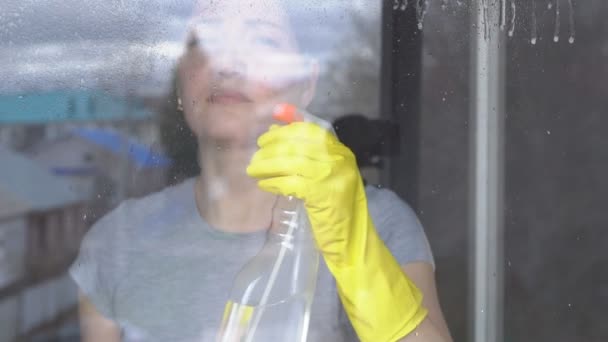Молода жінка миє вікно в жовтих рукавичках за допомогою засобу для чищення — стокове відео