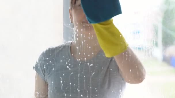 Schöne Frau wäscht Fenster mit blauem Lappen und Reinigungsmittel — Stockvideo