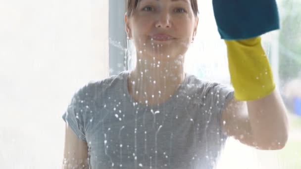 Όμορφη γυναίκα σε κίτρινα γάντια πλένει ένα παράθυρο με ένα πανί και ένα απορρυπαντικό — Αρχείο Βίντεο
