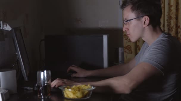 若い男がコンピューターで座っていると、食事のチップ — ストック動画