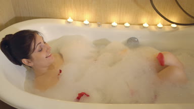 Esmer kadın köpük ve gül yaprakları ile banyo