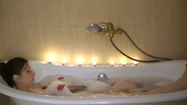 Молодая брюнетка принимает ванну при свечах — стоковое видео