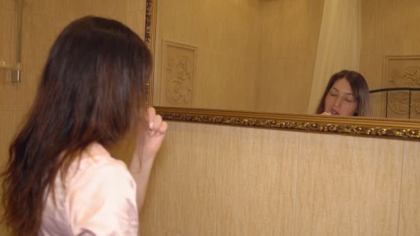 Mladá bruneta žena kartáčky na zuby před zrcadlem — Stock video