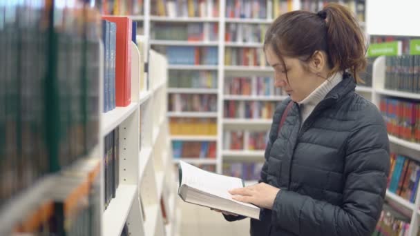 Брюнетка женщина в книжном магазине рассматривает книгу — стоковое видео