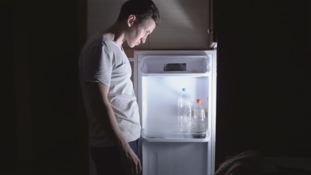 Joven comiendo por la noche cerca del refrigerador — Vídeo de stock