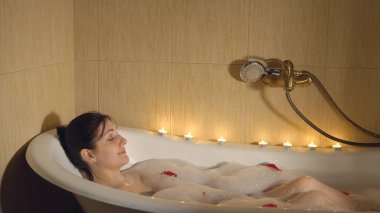 Köpük ve gül yaprakları ile mum ışığında banyo güzel kadın alır.