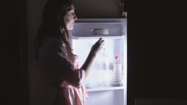 Молодая женщина ест ночью возле холодильника — стоковое видео