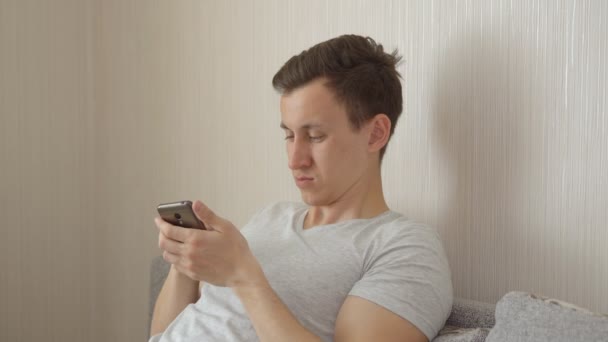 Young man is sitting on the couch with a phone — Stock Video