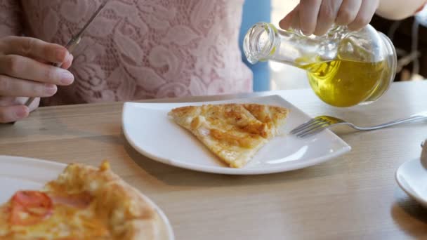 Junge Frau in einem Café isst Pizza und gießt Olivenöl ein — Stockvideo