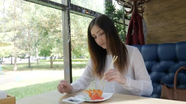 Jeune femme dans un café mange des rouleaux avec des bâtons de bois — Video