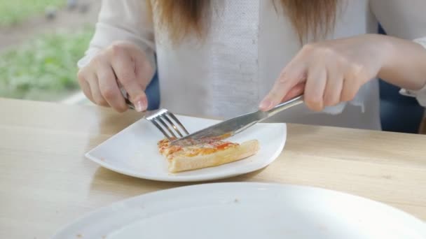 Een stukje pizza snijden met een mes en vork op een witte plaat — Stockvideo