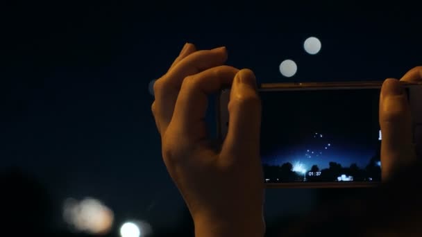 A woman shoots fireworks on a smartphone. Celebrating fireworks with Bokeh light background — Stock Video