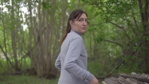 Молодая женщина бежит через лес, оглядываясь назад — стоковое видео