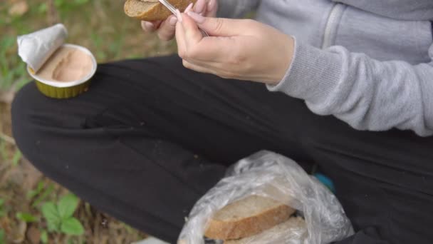 Mujer joven extiende paté en un pedazo de pan. Snack en la caminata — Vídeo de stock