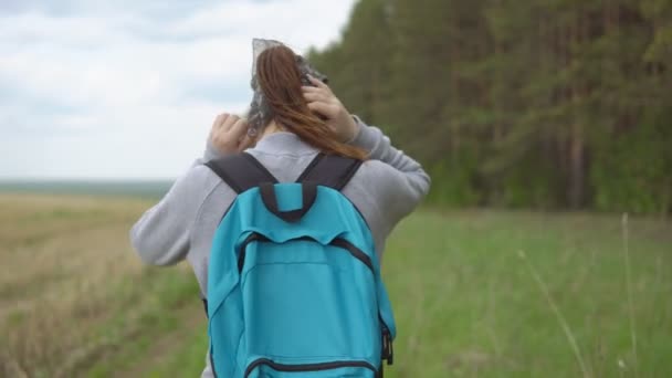 Mujer joven con una mochila en una caminata va entre el campo y el bosque — Vídeo de stock