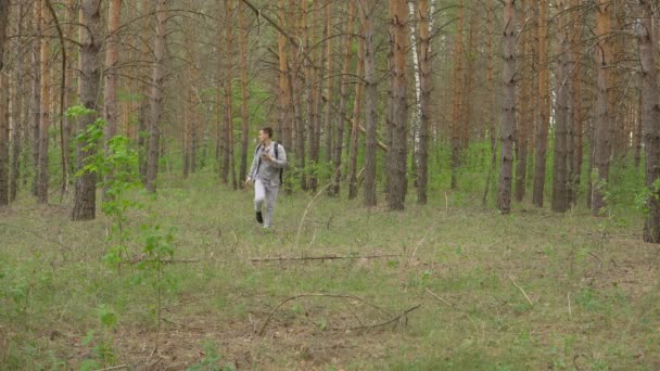 Молодой человек с рюкзаком ходит по лесу. Вид спереди — стоковое видео