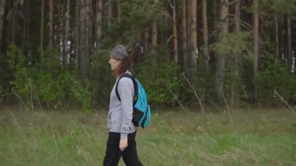 Jonge vrouw met een rugzak in een wandeling loopt langs een parcours op de achtergrond van een bos — Stockvideo
