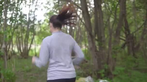 Mujer joven corriendo por el bosque, mirando hacia atrás — Vídeos de Stock