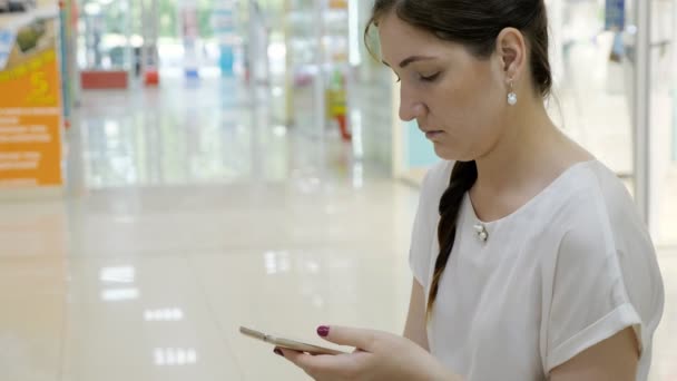 Jovem mulher se senta em um banco em um shopping com um telefone — Vídeo de Stock