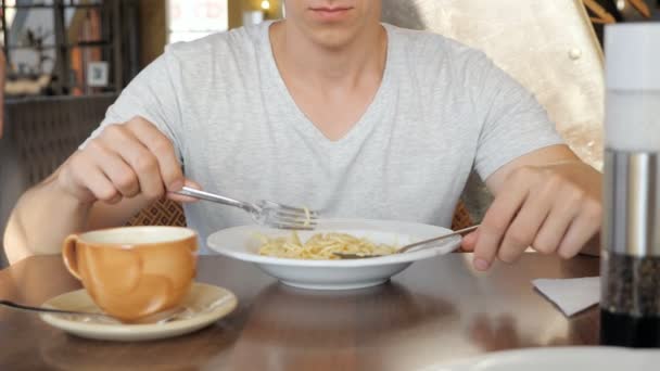 Молодой человек в кафе с аппетитом ест пасту — стоковое видео