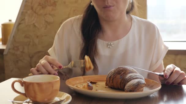 Mujer joven come croissant y canta café en la cafetería — Vídeos de Stock