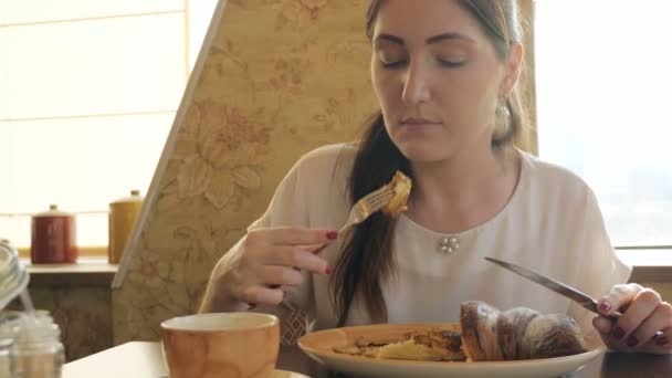 Brunette vrouw eten van een croissant en zingen koffie in een café — Stockvideo