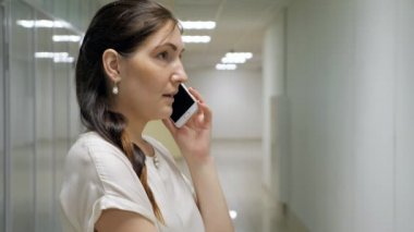 Genç kadın bir ofis binası koridorunda telefonda söz