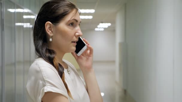 Jonge vrouw praten over de telefoon in de hal van een kantoorgebouw — Stockvideo