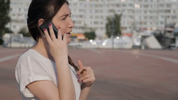 Morena mujer en la calle está dejando caer un teléfono mientras habla — Vídeo de stock