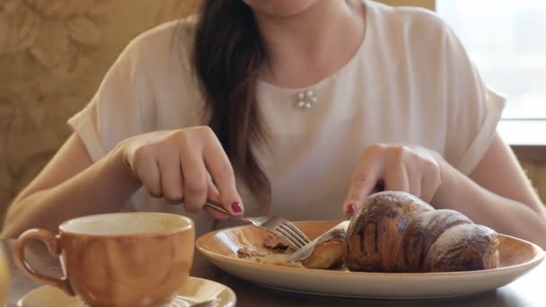 Brunette femme manger un croissant et chanter du café dans un café — Video