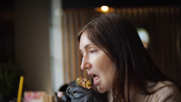 カフェでハンバーガーを食べる黒い手袋の若い女の子の側面図 — ストック動画