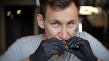 Genç bir adam siyah eldiven bir kafede hamburger yemek