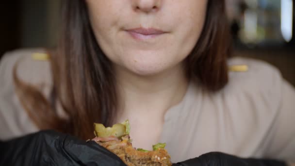 Nahaufnahme eines unbekannten Mädchens in schwarzen Handschuhen, das in einem Café einen Burger isst — Stockvideo