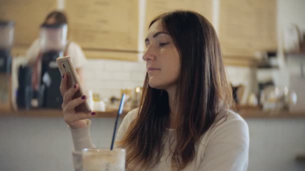 Κορίτσι γραπτών μηνυμάτων για το έξυπνο τηλέφωνο σε ένα εστιατόριο με ένα υπόβαθρο αόριστες. — Αρχείο Βίντεο