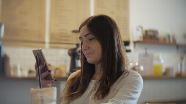 Молодая женщина в кафе пьет кофе и пользуется мобильным телефоном — стоковое видео