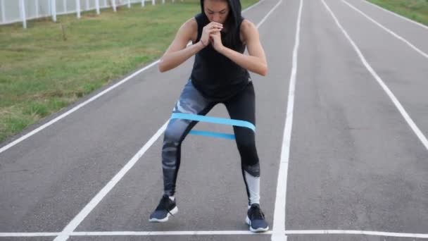 Menina desportiva fazendo exercícios de perna com faixa de borracha fitness — Vídeo de Stock